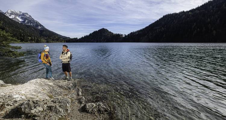 Deux randonneurs debout à côté d'un lac limpide entouré de montagnes.
