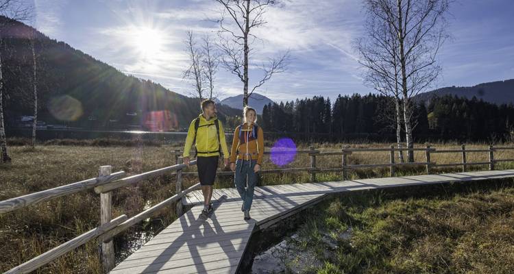 Un couple marchant sur un sentier en bois avec un paysage montagneux en arrière-plan.