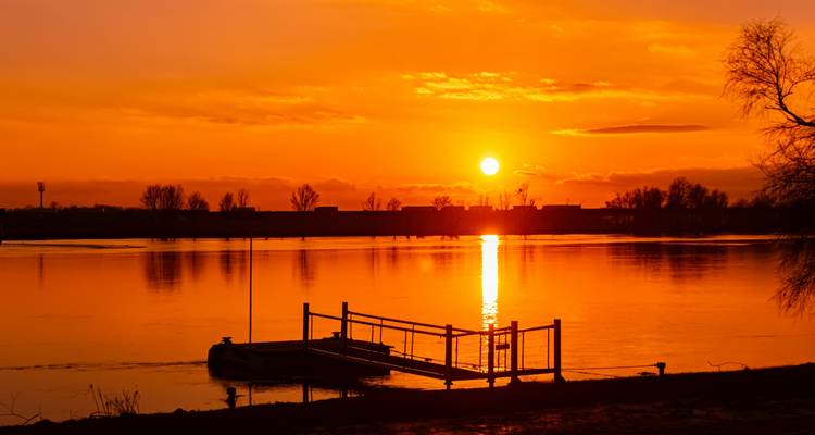 Sonnenuntergang über einem Fluss mit einem leuchtend orangefarbenen Himmel.