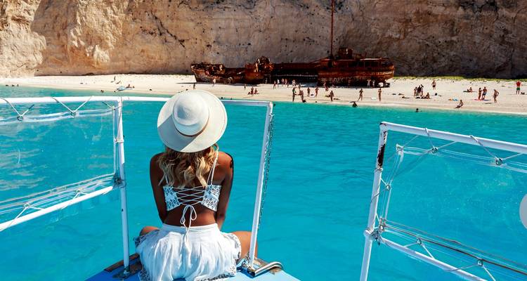 Person, die auf einem Boot sitzt und dem Schiffswrack am Navagio Beach zugewandt ist.