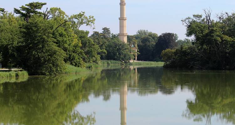 Un minaret élevé se reflétant dans une rivière calme aux rives bordées d'arbres.