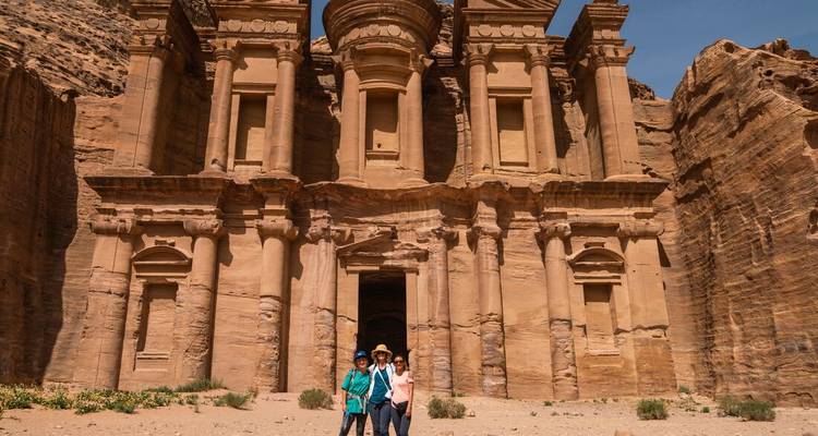 Visitors standing before grand façade of Petra Monastery carved into sandstone cliff