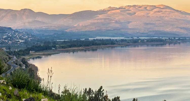 Landschapsaanzicht van een kalm meer met verre heuvels bij zonsondergang.