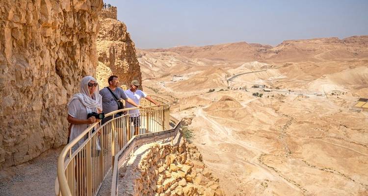 Toeristen op een loopbrug met uitzicht op een uitgestrekt rotsachtig woestijnlandschap.