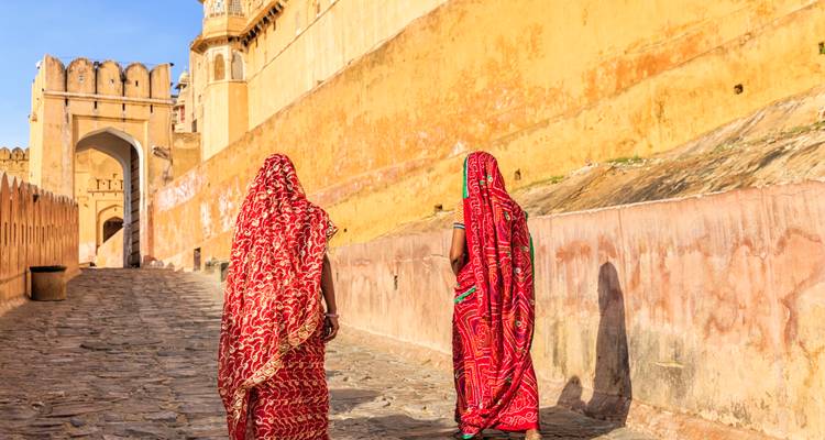 Dos mujeres en saris rojos vibrantes caminan por las murallas empedradas de los muros ocres del Fuerte Amber.