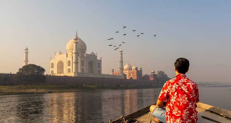 Viajero en bote en el río Yamuna observa el amanecer sobre el Taj Mahal con una bandada de pájaros sobre el mausoleo.