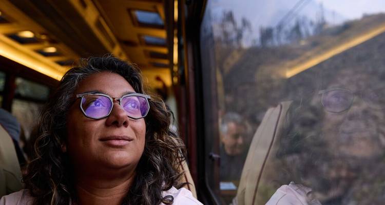 Mujer mira por la ventana de un tren, reflejos del paisaje montañoso visibles en el cristal.