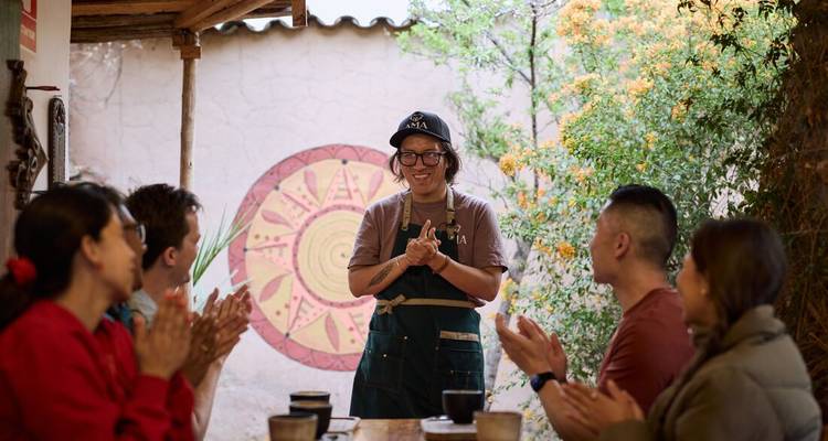 Un pequeño grupo aplaude a un chef local sonriente durante una demostración de cocina interactiva en un patio abierto.