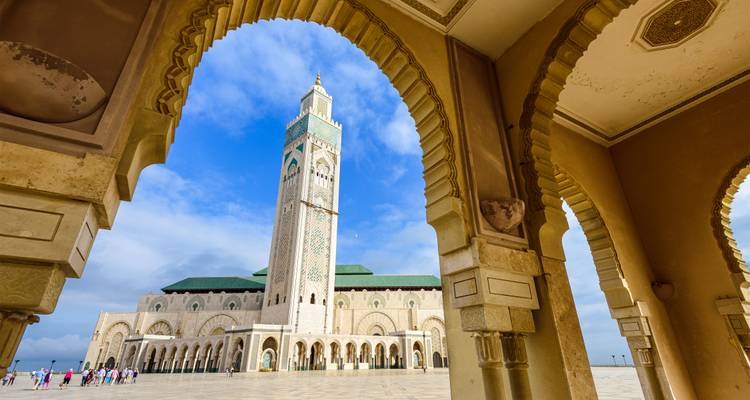 Mezquita de Hassan II enmarcada por arcos de piedra ornamentados bajo un cielo azul brillante de Casablanca.