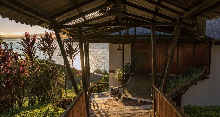 Covered wooden walkway overlooking a serene river and tropical foliage in late afternoon light.