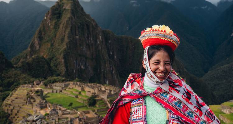Lächelnde Frau in farbenfroher Quechua-Kleidung steht vor den majestätischen Ruinen von Machu Picchu.