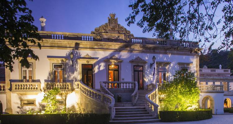 Elegante mansión histórica suavemente iluminada al atardecer con una gran escalera y jardín bien cuidado.