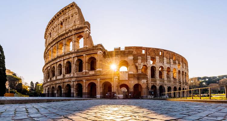 El Coliseo resplandeciendo con la luz del amanecer, rayos de sol atravesando los arcos antiguos y el primer plano de adoquines
