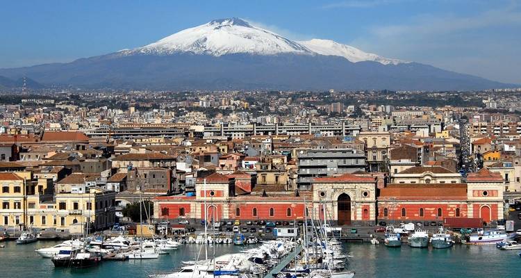 Stadtansicht mit einem Hafen und dem Ätna im Hintergrund.