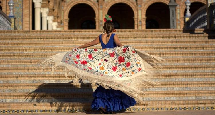 Mujer con vestido tradicional frente a un edificio histórico en Sevilla.