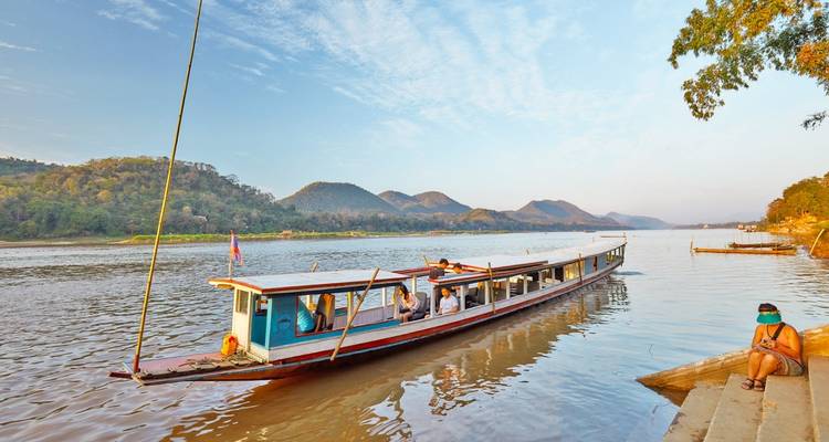 Langes traditionelles Boot auf einem ruhigen Fluss mit Bergen im Hintergrund.