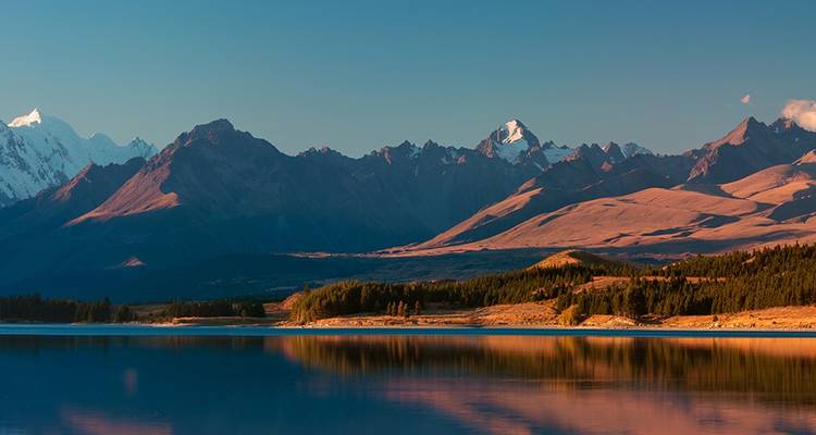 Tranquilo lago alpino en la hora dorada reflejando la cadena montañosa distante con un cielo despejado.