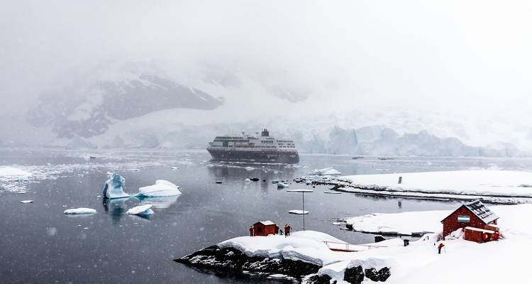 A cruise ship near a snowy shore with small buildings and icebergs.