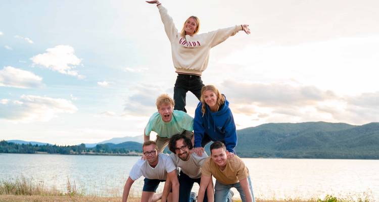 Groep jonge mensen die een menselijke piramide vormen bij een meer.