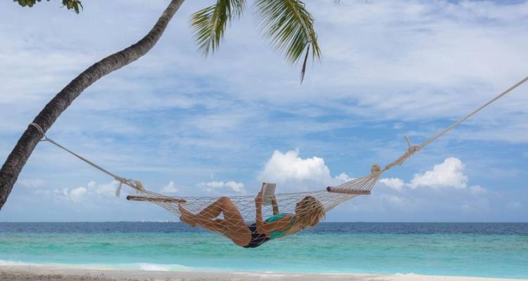 Une personne se détendant dans un hamac entre des palmiers sur une plage.