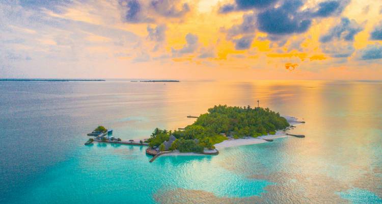 Petite île aux Maldives au coucher du soleil avec des reflets vibrants du ciel.