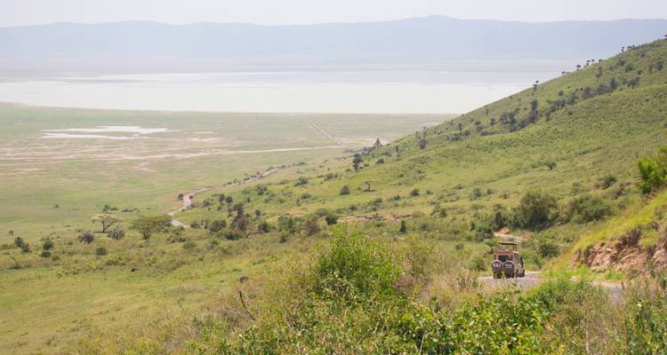 Paysage vallonné avec un véhicule sur un chemin de terre en pente vers un lac.