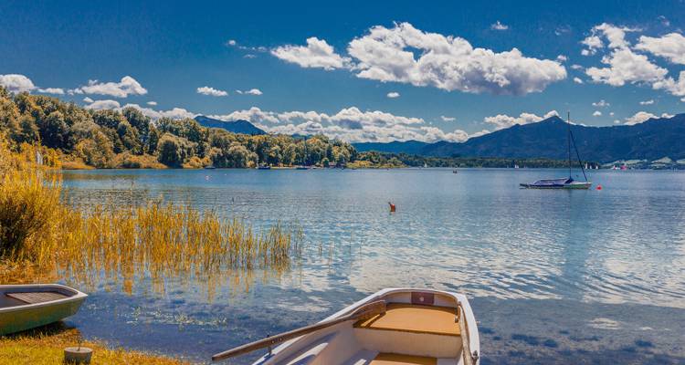 Meer met boten en verre bergen onder een blauwe hemel.