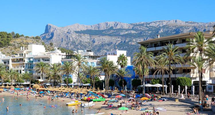 Une plage animée avec des gens qui se détendent, des palmiers et des montagnes en arrière-plan.