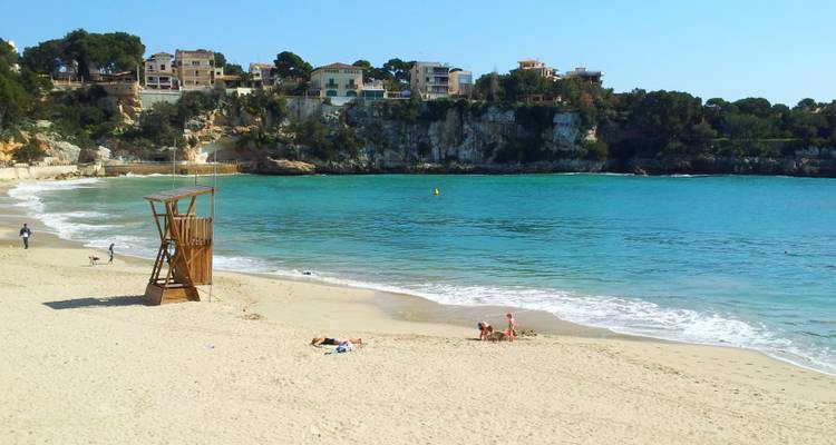 Une plage avec un poste de secours en bois et quelques personnes profitant du sable et de la mer.