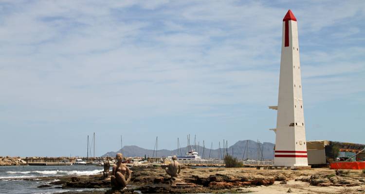 Un phare avec un sommet pointu entouré d'un terrain rocheux et de la mer.