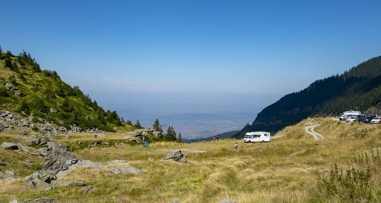 Col de montagne avec des véhicules garés et des personnes profitant de la vue.