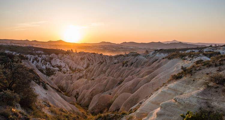 Un paysage aride et rocheux avec le soleil qui se couche en arrière-plan.