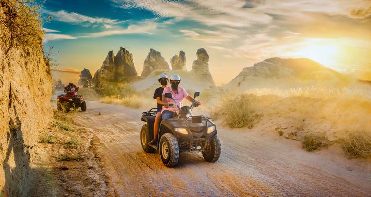 People riding quad bikes on a dirt road with sandstone formations in the background.