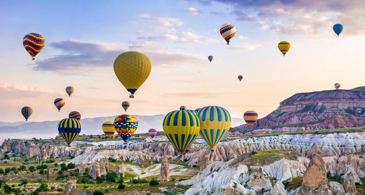 Multiple hot air balloons flying over the landscapes of Cappadocia.