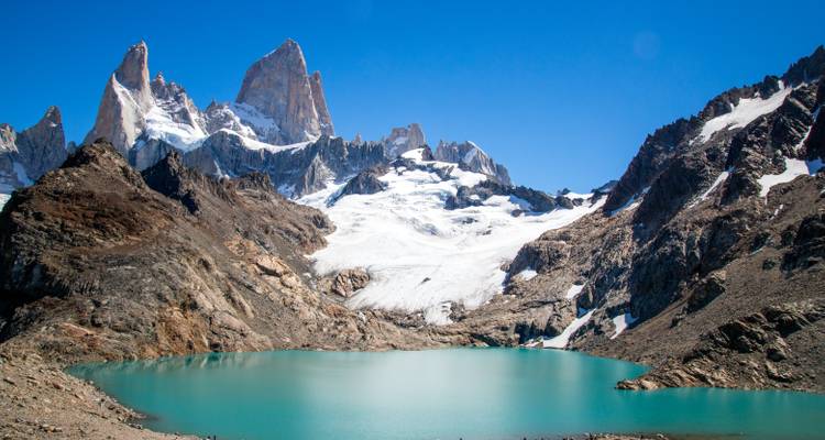 Turkooise gletsjermeer omringd door de ruige besneeuwde toppen van Mount Fitz Roy onder een heldere blauwe Patagonische hemel.