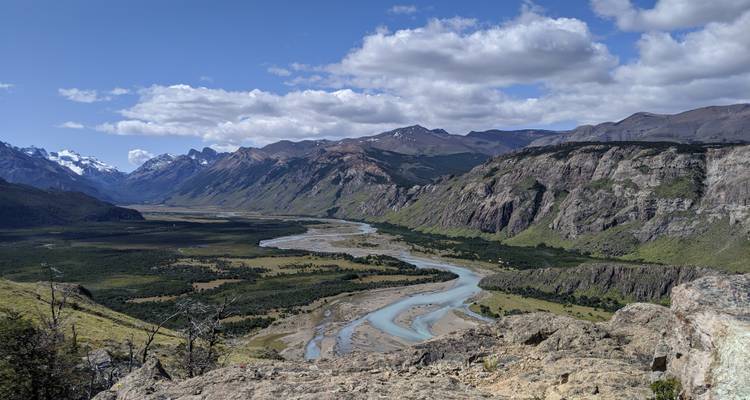 Uitgestrekte vallei met een kronkelende turquoise rivier, omgeven door dramatische Andean gebergten onder een gedeeltelijk bewolkte hemel.