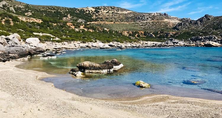 Plage isolée avec une eau bleue claire et un terrain rocheux.