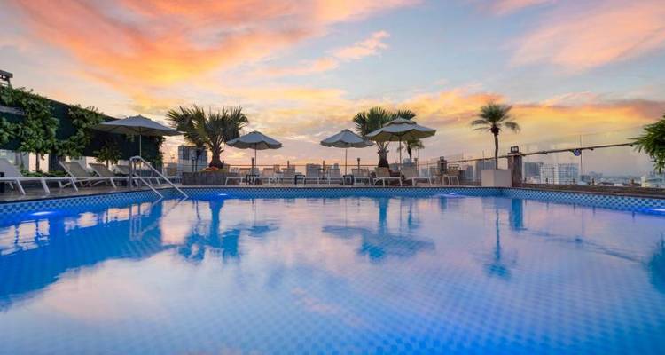 Piscina en la azotea con vista al atardecer y plantas tropicales.