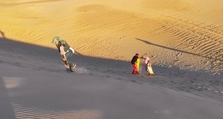 Persoon die met metgezellen een zandige heuvel afglijdt.