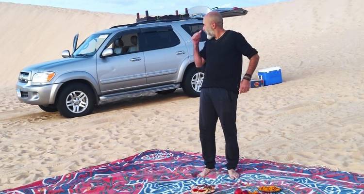 Persoon die staat op een gedessineerde deken naast een SUV in de woestijn.