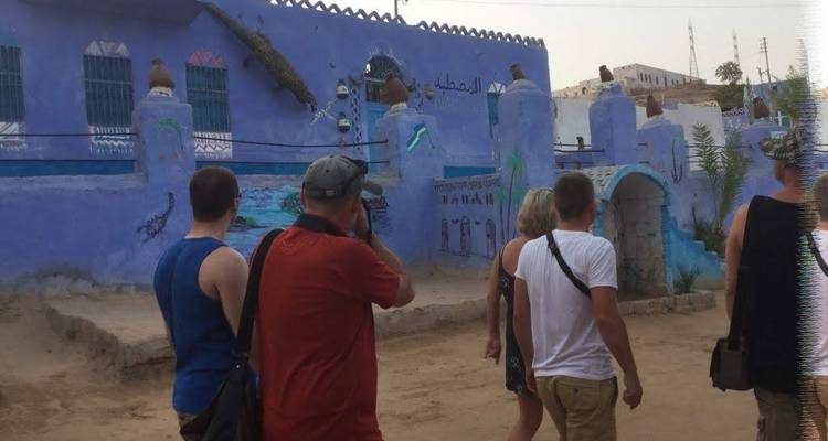 Toeristen die langs levendige blauw gedecoreerde muren in een klein dorp lopen.