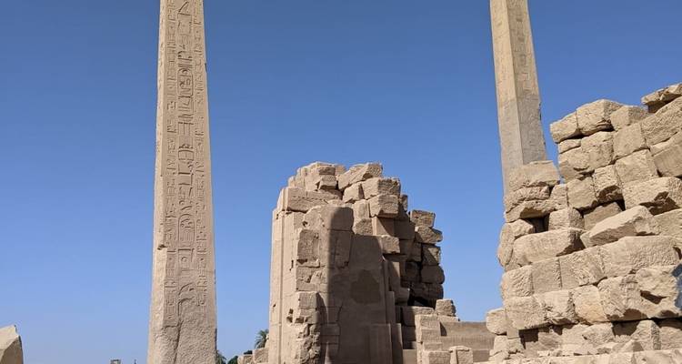 Ruïnes met hoge obelisk en oude stenen blokken.