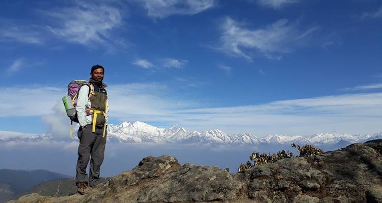 Ein Wanderer, der auf einem felsigen Bergrücken steht, mit schneebedeckten Bergen im Hintergrund.