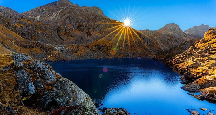 Ein unberührter Bergsee, der die Sonne widerspiegelt mit leuchtenden Farben der umliegenden Felsen.