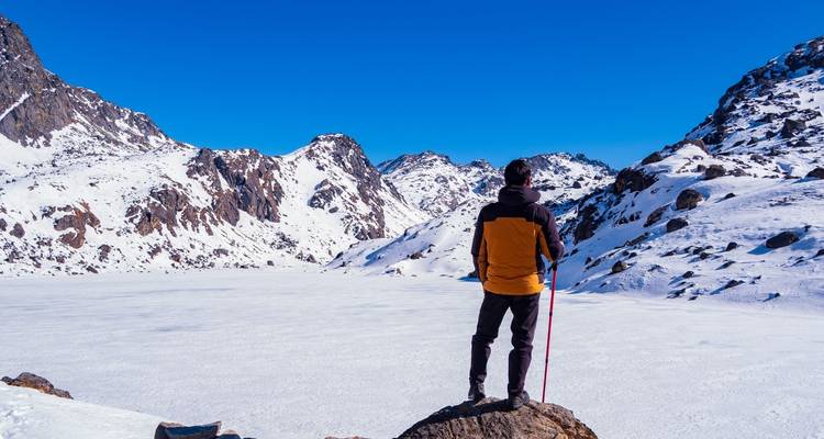 Eine Person, die auf einem schneebedeckten Gipfel steht und auf einen zugefrorenen See blickt.