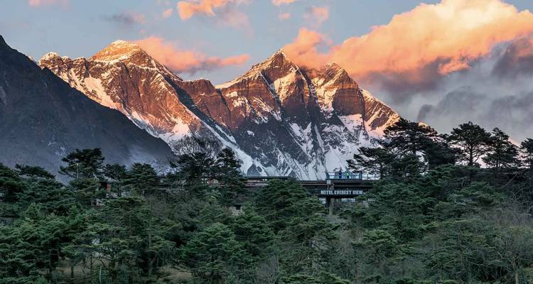 Un hôtel au milieu d'une forêt surplombant les montagnes au coucher du soleil.