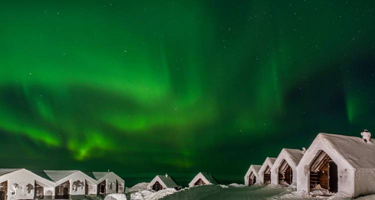Aurores boréales au-dessus de cabanes enneigées la nuit.