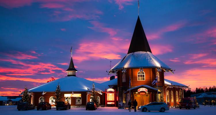 Bâtiment couvert de neige avec des lumières sous un ciel de coucher de soleil.