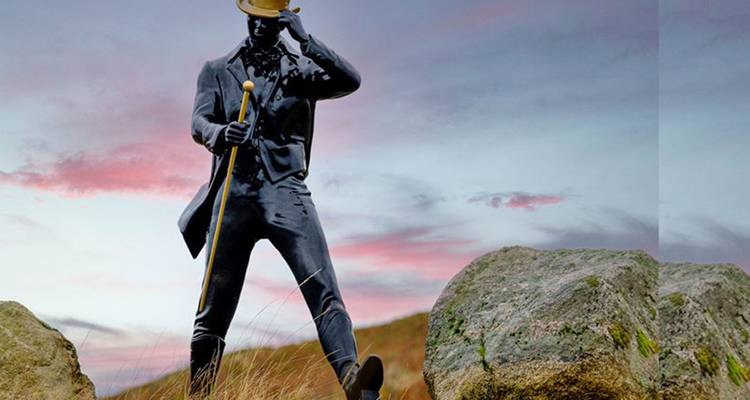 Estatua de un hombre caminando con bastón contra un cielo colorido.