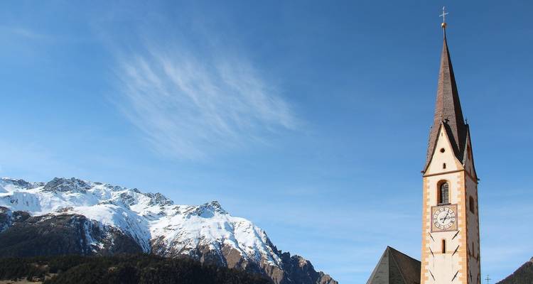 Un clocher d'église qui se dresse sur un fond de montagnes enneigées.